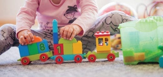 Child playing with a colorful toy train made of building blocks on the floor.