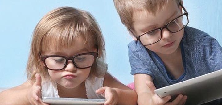 Two children wearing glasses look at tablets.