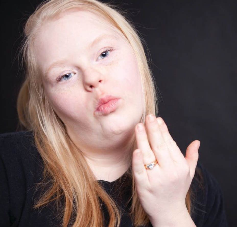 Angel with blonde hair and a black shirt puckers her lips and blows a kiss.