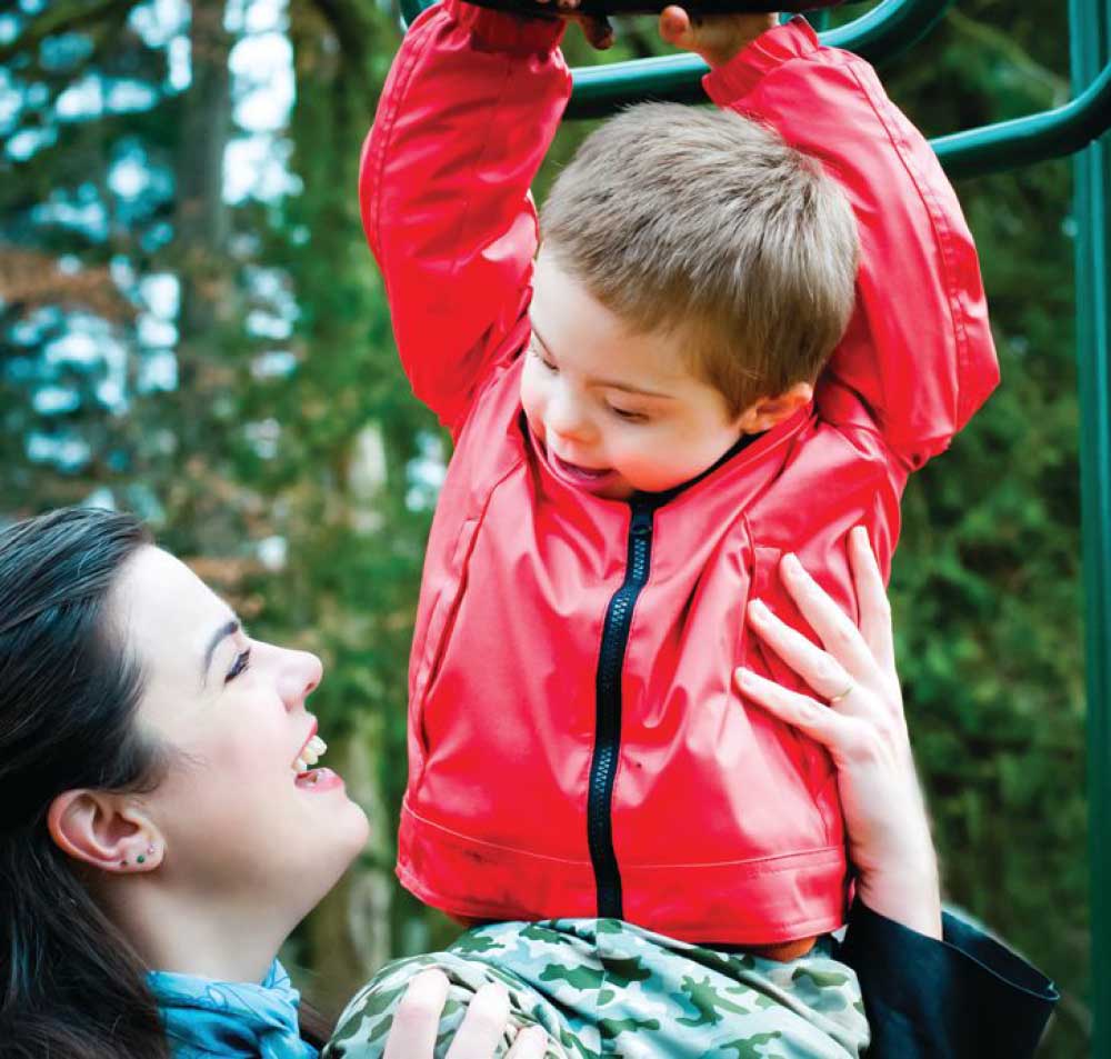 Connor smiles while being held by a woman at a playground.
