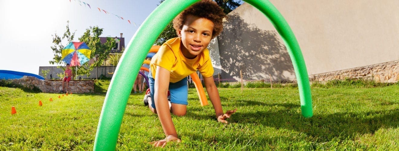 Child crawls through green obstacle in a backyard