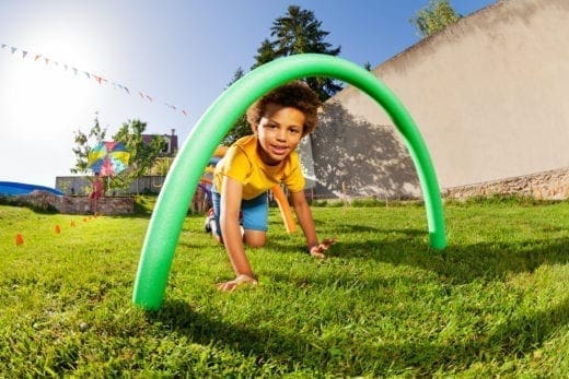 Child crawls through green obstacle in a backyard