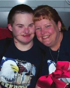 Seth and his mother smile together, with a red bow in the foreground.