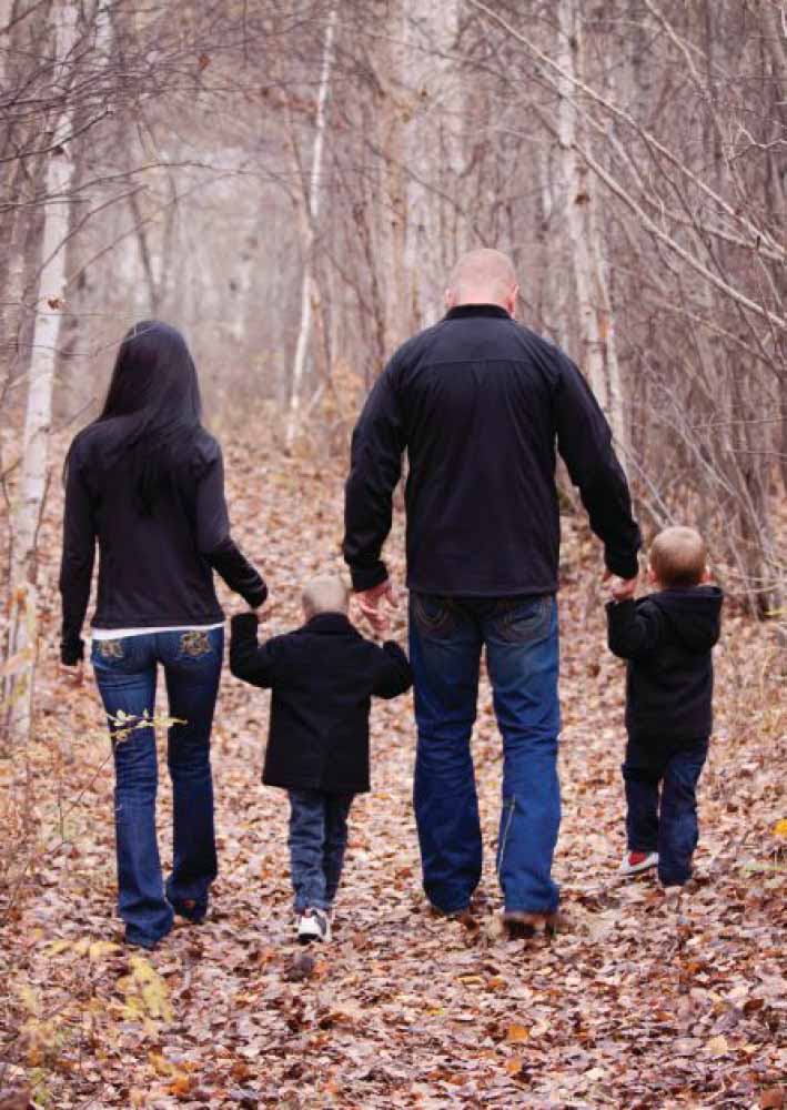 Family walking on a leaf-covered path in a wooded area.