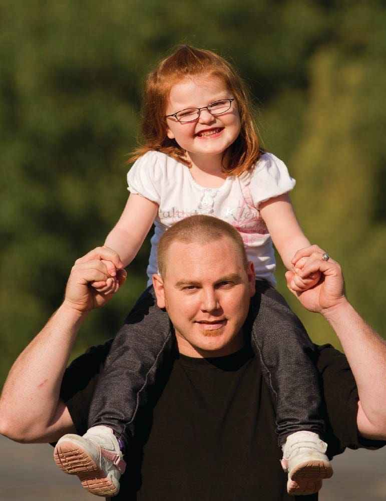 Kylie rides on her dad's shoulders outdoors.