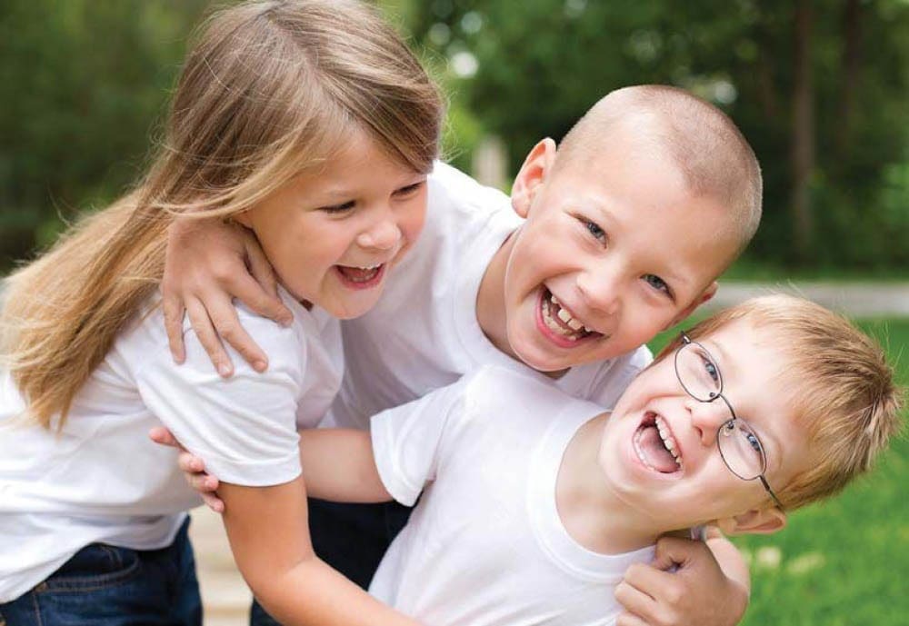 Three children laughing together outdoors.