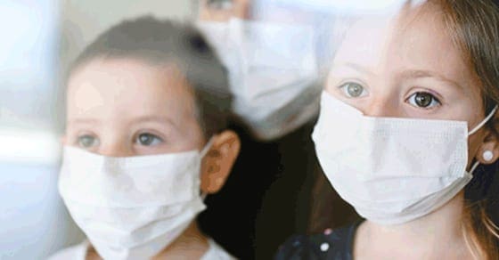 Children in medical masks look out a window.
