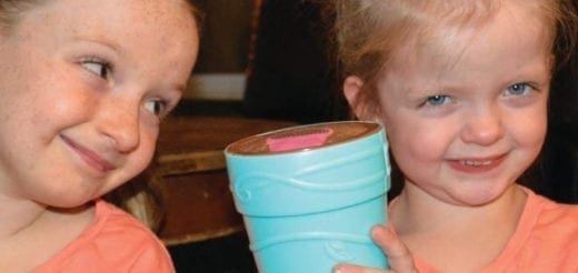 Two children smile as they hold a blue toy.