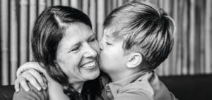 A boy kisses a woman on the cheek as she smiles.