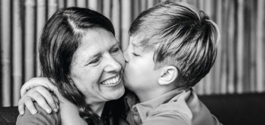 A boy kisses a woman on the cheek as she smiles.