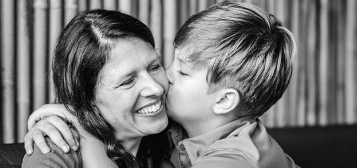 A boy kisses a woman on the cheek as she smiles.