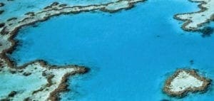 Aerial view of a heart-shaped coral reef in a bright blue ocean.