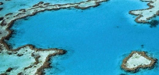 Aerial view of a heart-shaped coral reef in a bright blue ocean.