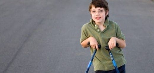 A boy with a walker stands on pavement.