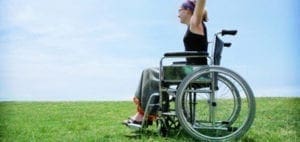 A person in a wheelchair raises their arms against a blue sky.