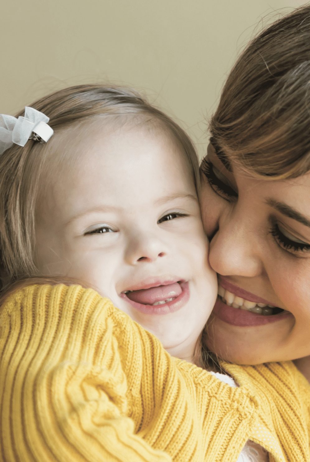 A woman hugs a smiling child with Down syndrome.