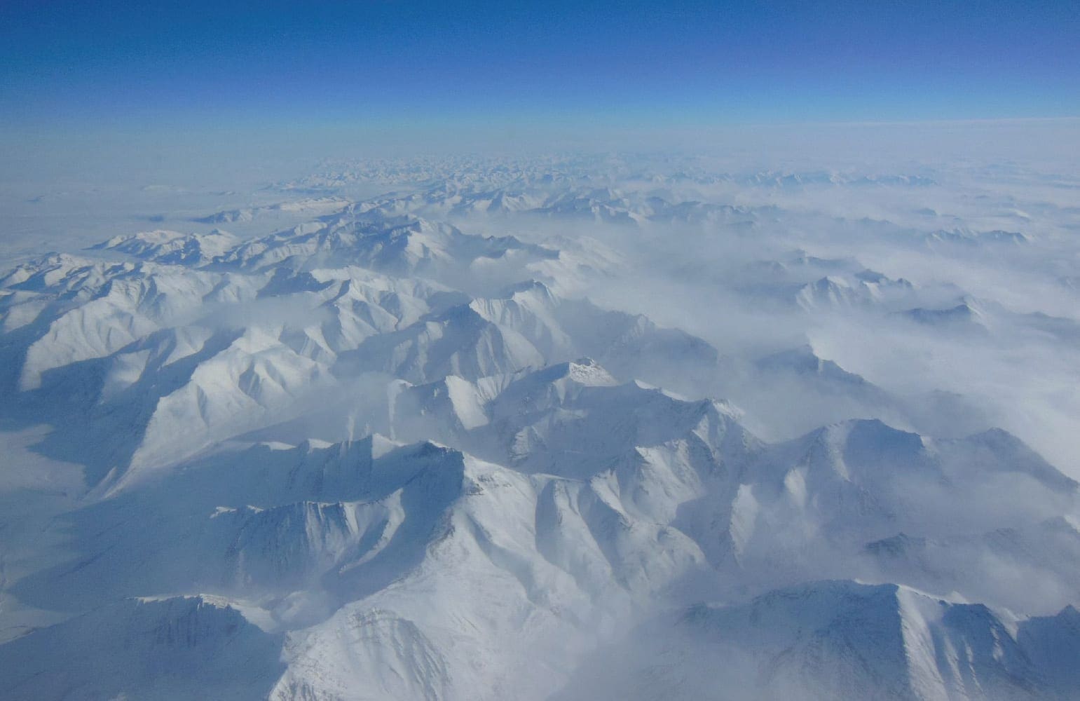 Snow-covered Alaskan mountains seen from above under a clear blue sky.