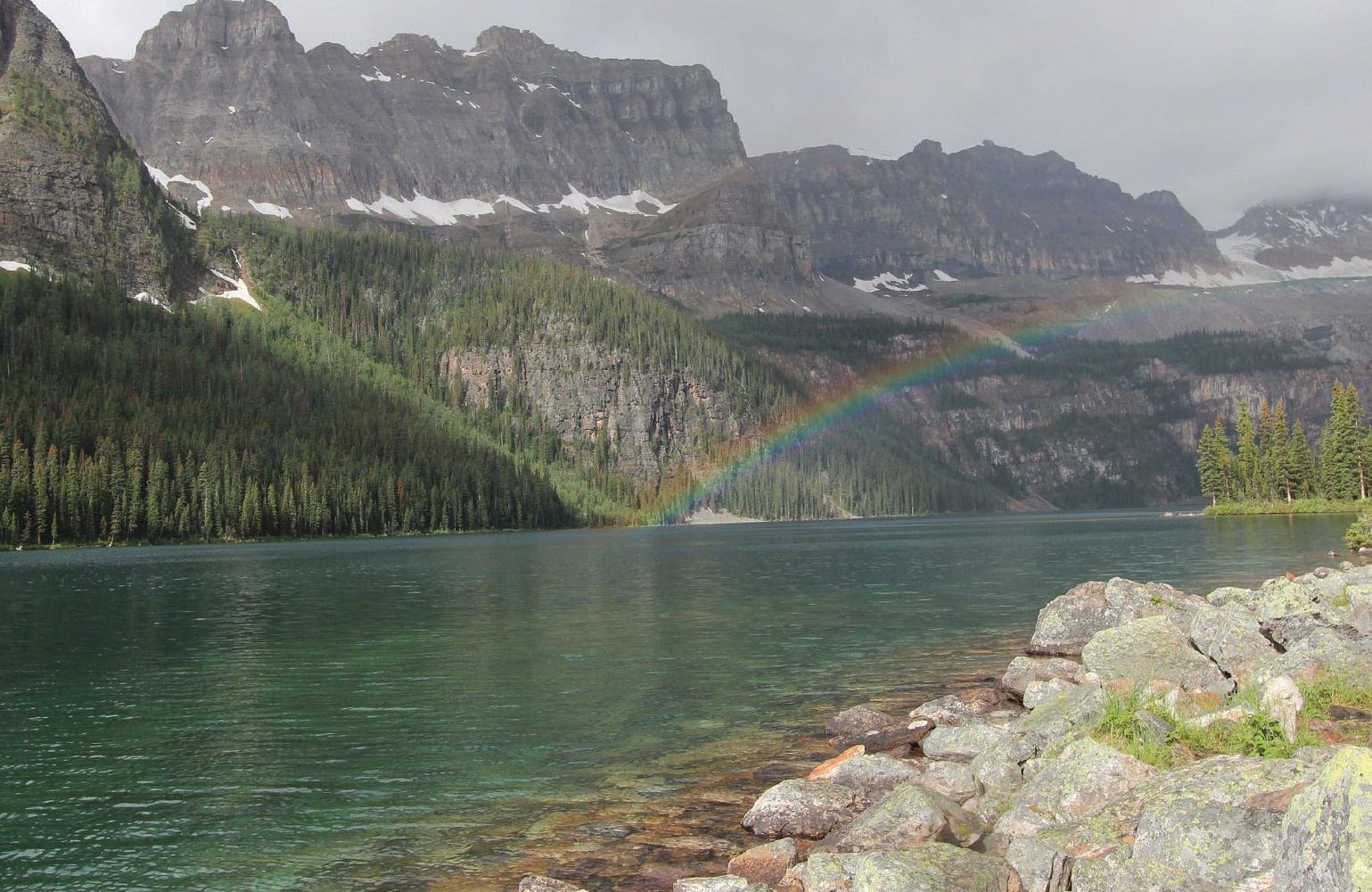 Boom Lake in Alberta, Canada, with a rainbow over the water and mountains in the background.