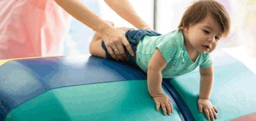 Baby on a blue and green bolster with hands supporting their back.