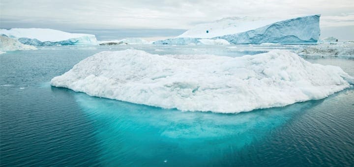 Arctic icebergs floating in turquoise water under a cloudy sky.