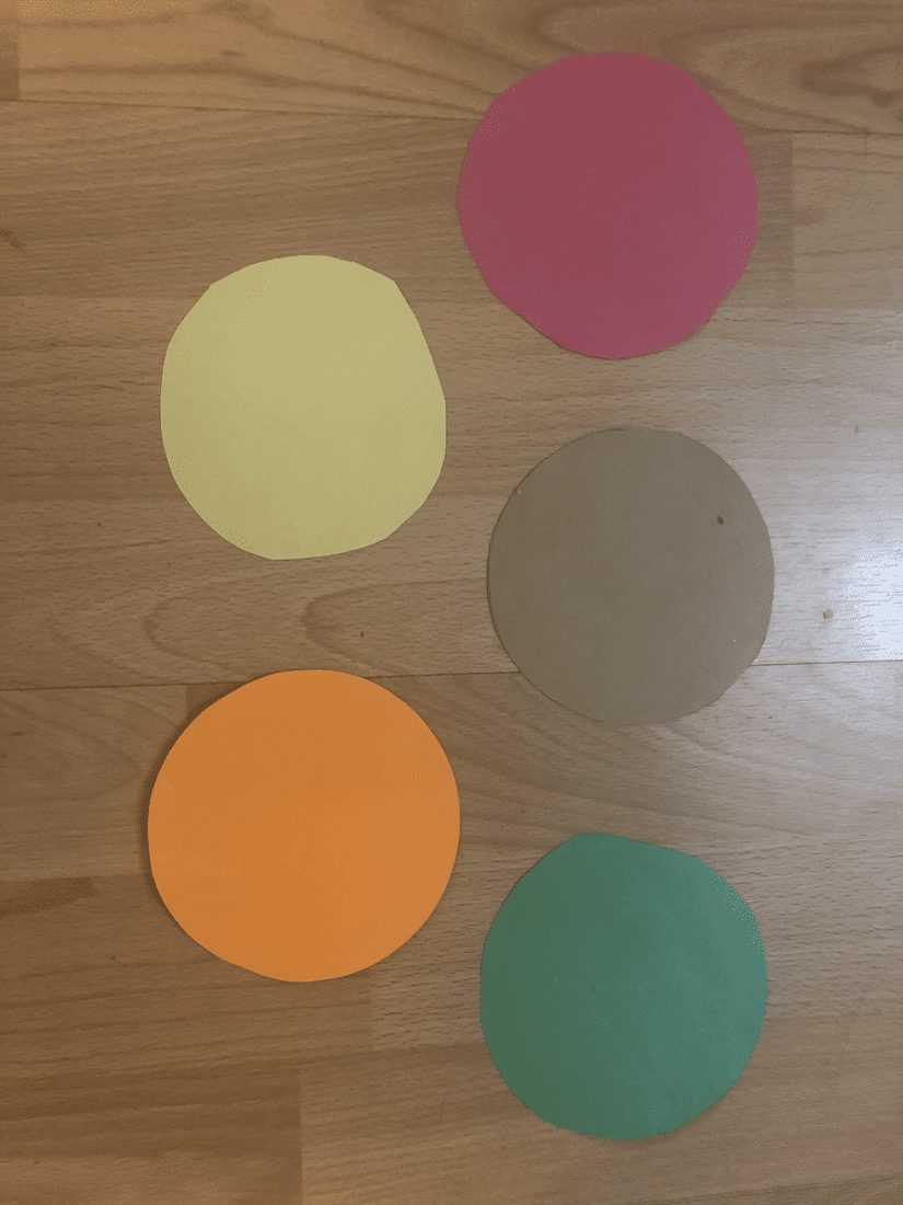 Five colored paper circles arranged on a wooden surface.