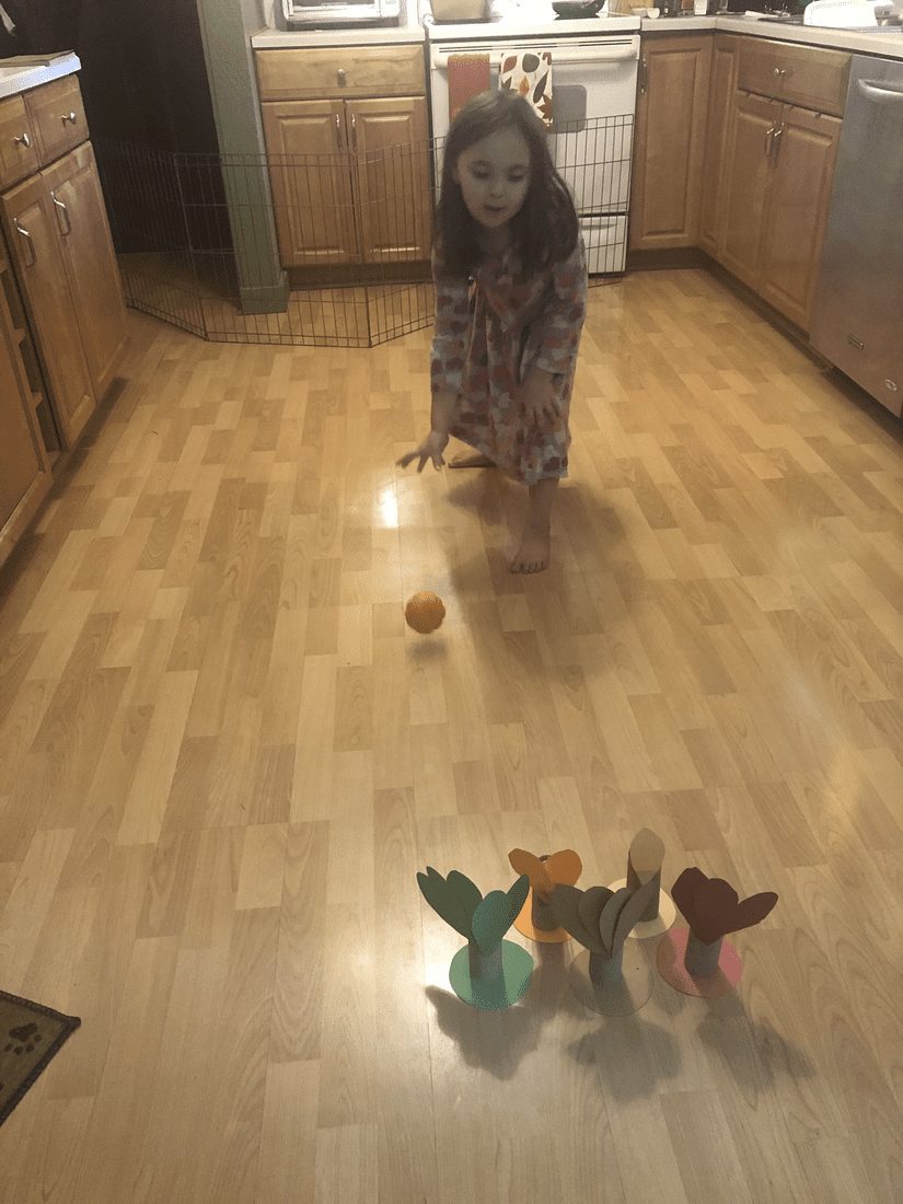 A young girl prepares to roll a small ball at homemade turkey bowling pins.