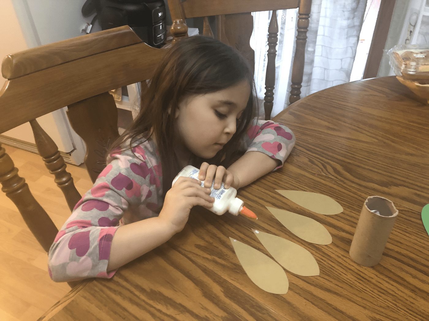 Girl gluing feathers onto toilet paper tube for turkey bowling craft