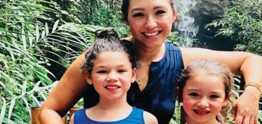 Lisa Pena smiling with two young girls in front of lush greenery.