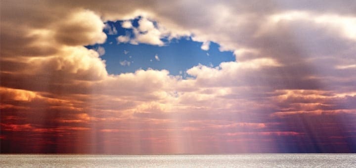 Sunrise over the ocean with dramatic clouds and light rays.