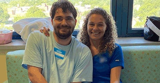 Man and woman smiling together in front of a window.