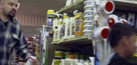 Man in a plaid shirt walking past shelves of products.