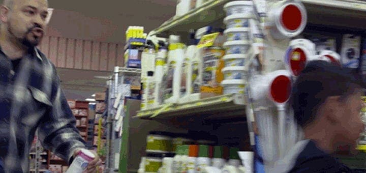 Man in a plaid shirt walking past shelves of products.