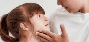 A child looks up at an adult who is touching their face.