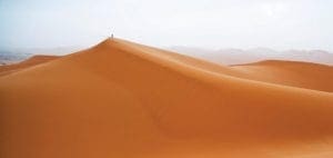 Person stands atop a sand dune in Erg Chebbi, Morocco.