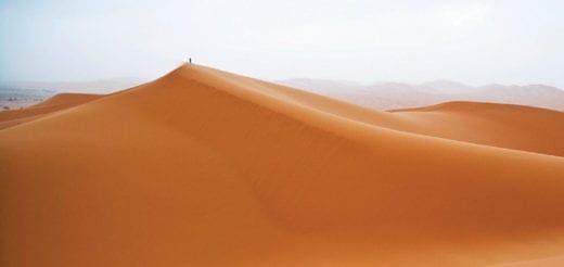 Person stands atop a sand dune in Erg Chebbi, Morocco.