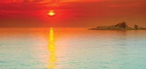 Sunset over the ocean with a small island on the horizon