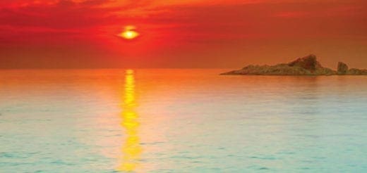Sunset over the ocean with a small island on the horizon