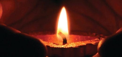 A candle flame glows warmly, with dark shapes framing the light.