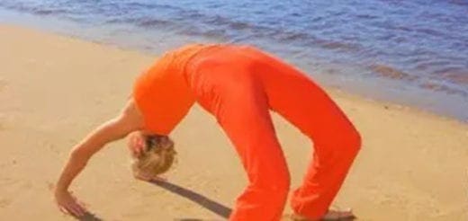 Person in orange doing a backbend yoga pose on a sandy beach.