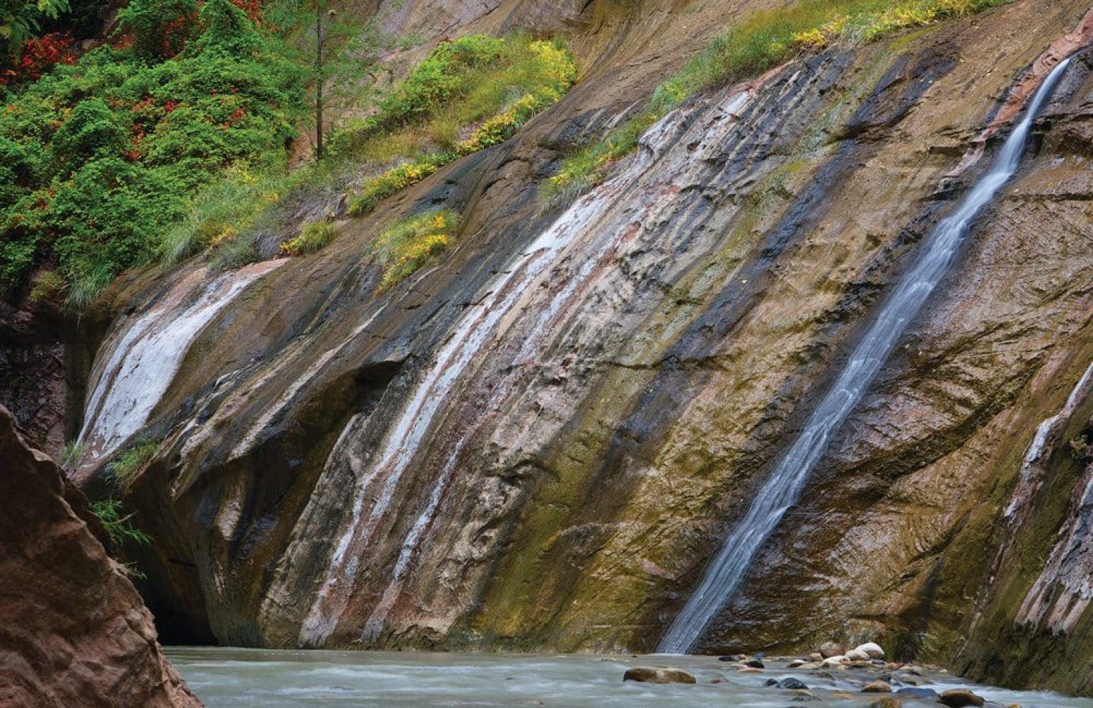 Run-off water streams down the stained sandstone canyon walls into a river in Zion National Park.