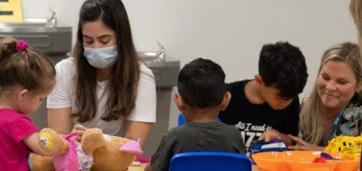 Adults work with children at tables during a hybrid early intervention program activity.