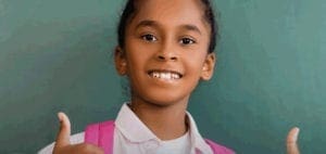 Young girl gives two thumbs up in front of a chalkboard