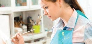 Young woman in an artist's smock painting on a canvas