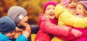 Children in colorful coats and hats hug each other and laugh.