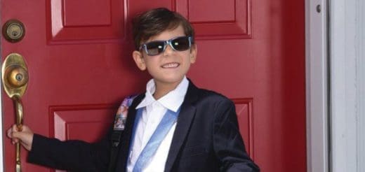 Alec in a suit and sunglasses stands by a red door.