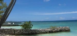 Stone wall in foreground with calm turquoise water and blue sky.