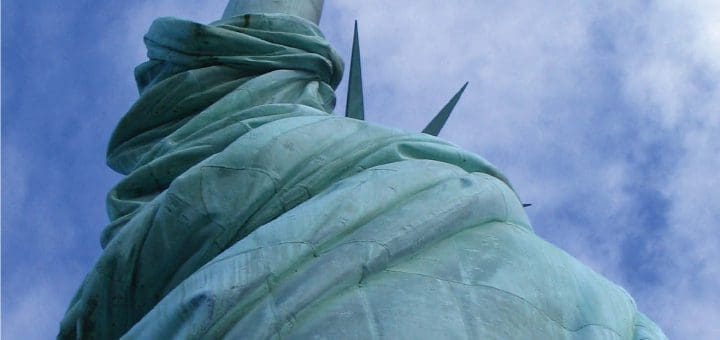 Back of the Statue of Liberty against a blue sky with clouds.