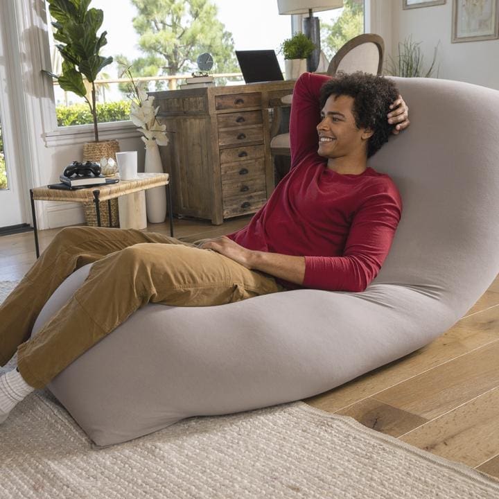 Person relaxing on a Yogibo Max bean bag chair that conforms to their body shape in a sunlit living room.