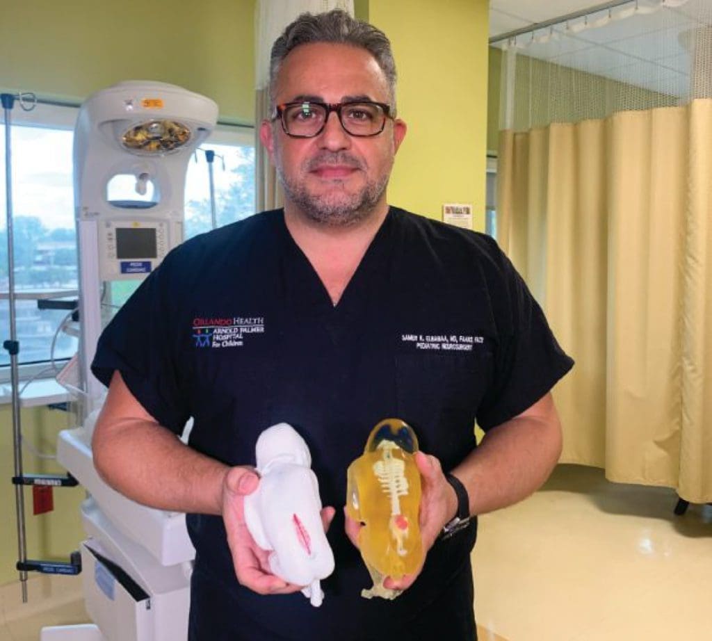 Man in scrubs holding two 3D printed models in a medical setting.