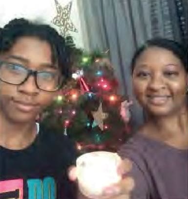 A young person and a woman smile in front of a Christmas tree.